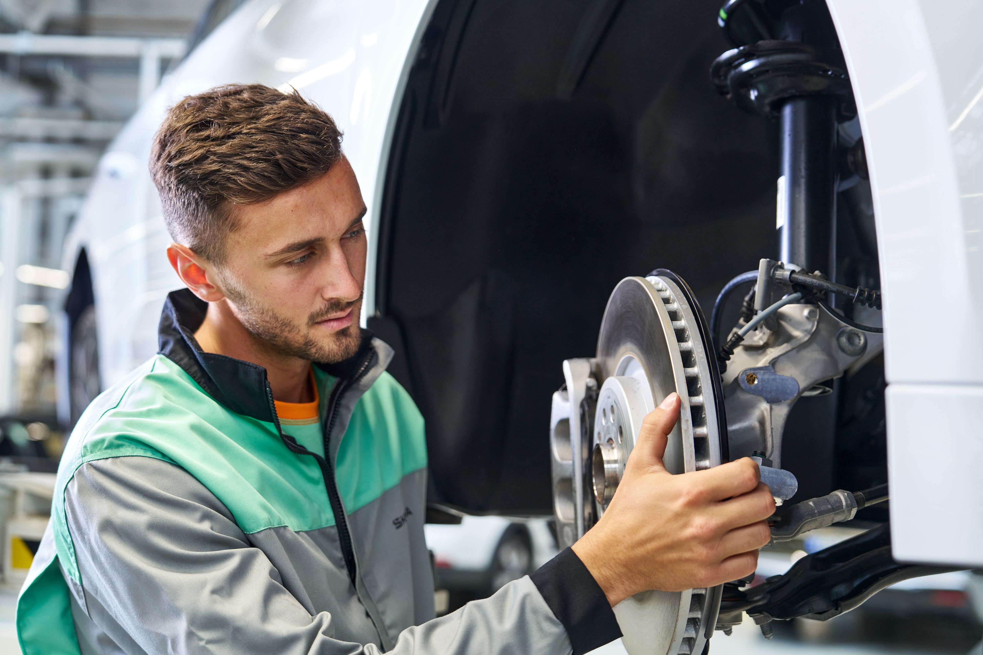 Avtomehanik preverja zavorni sistem avtomobila, pri čemer drži zavorni disk in pregleduje komponento pod dvignjenim vozilom.