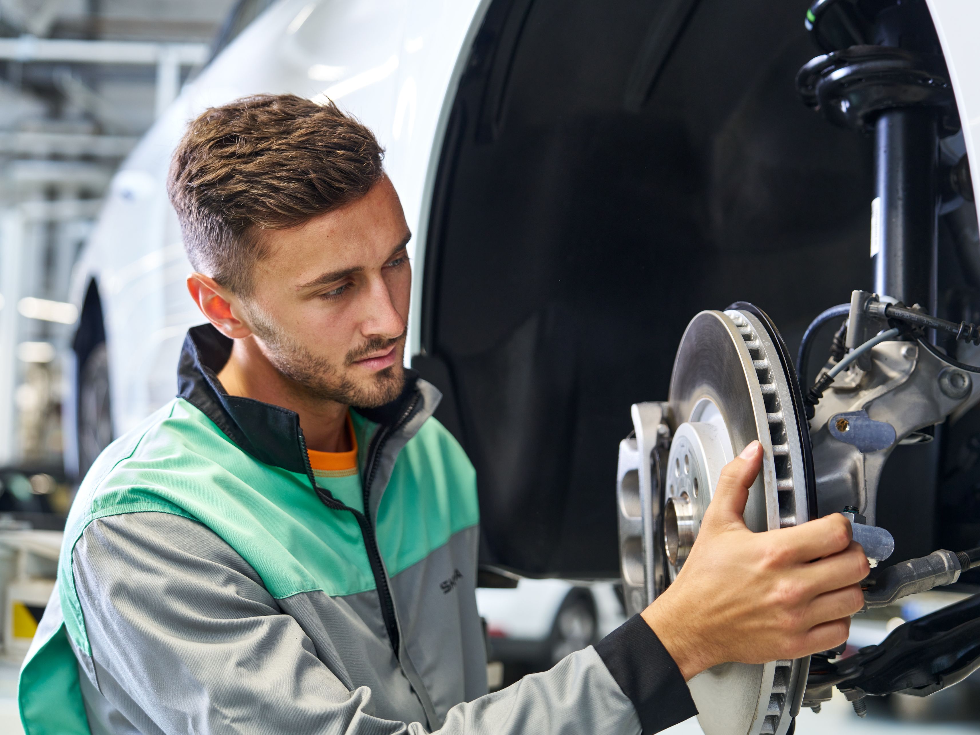 Avtomehanik preverja zavorni sistem avtomobila, pri čemer drži zavorni disk in pregleduje komponento pod dvignjenim vozilom.