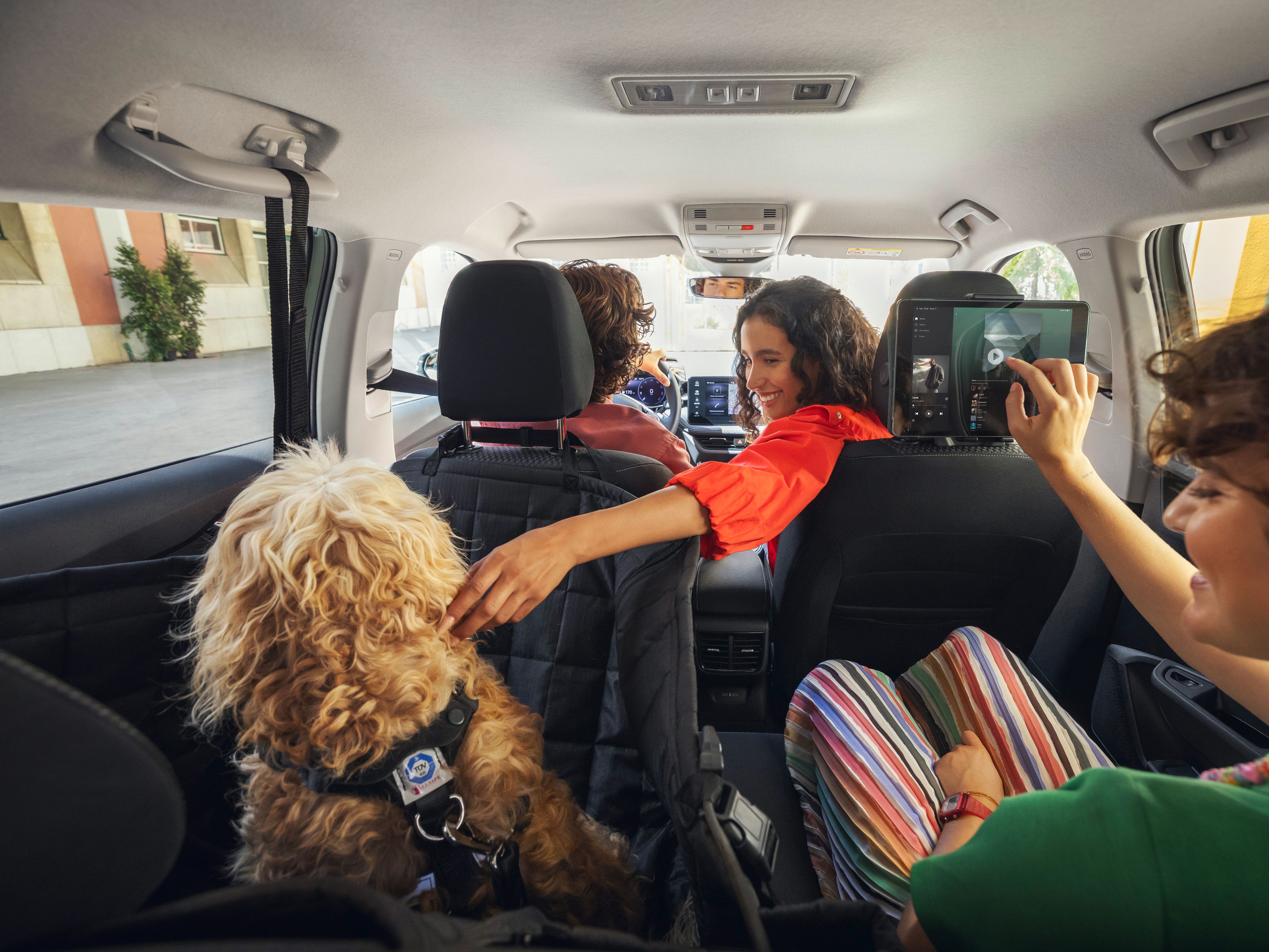 Tri osebe in en kuža sedijo v vozilu Škoda in se vozijo po cesti