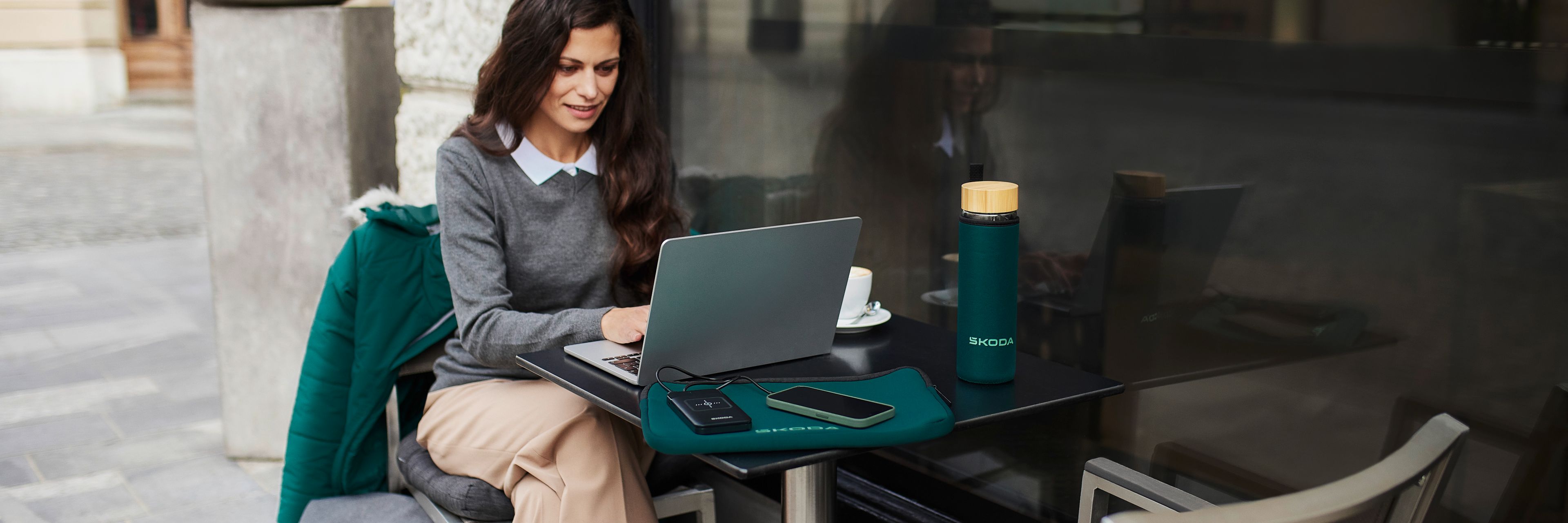 Ženska sedi za mizo pred kavarno na ulici, tipka na laptopu