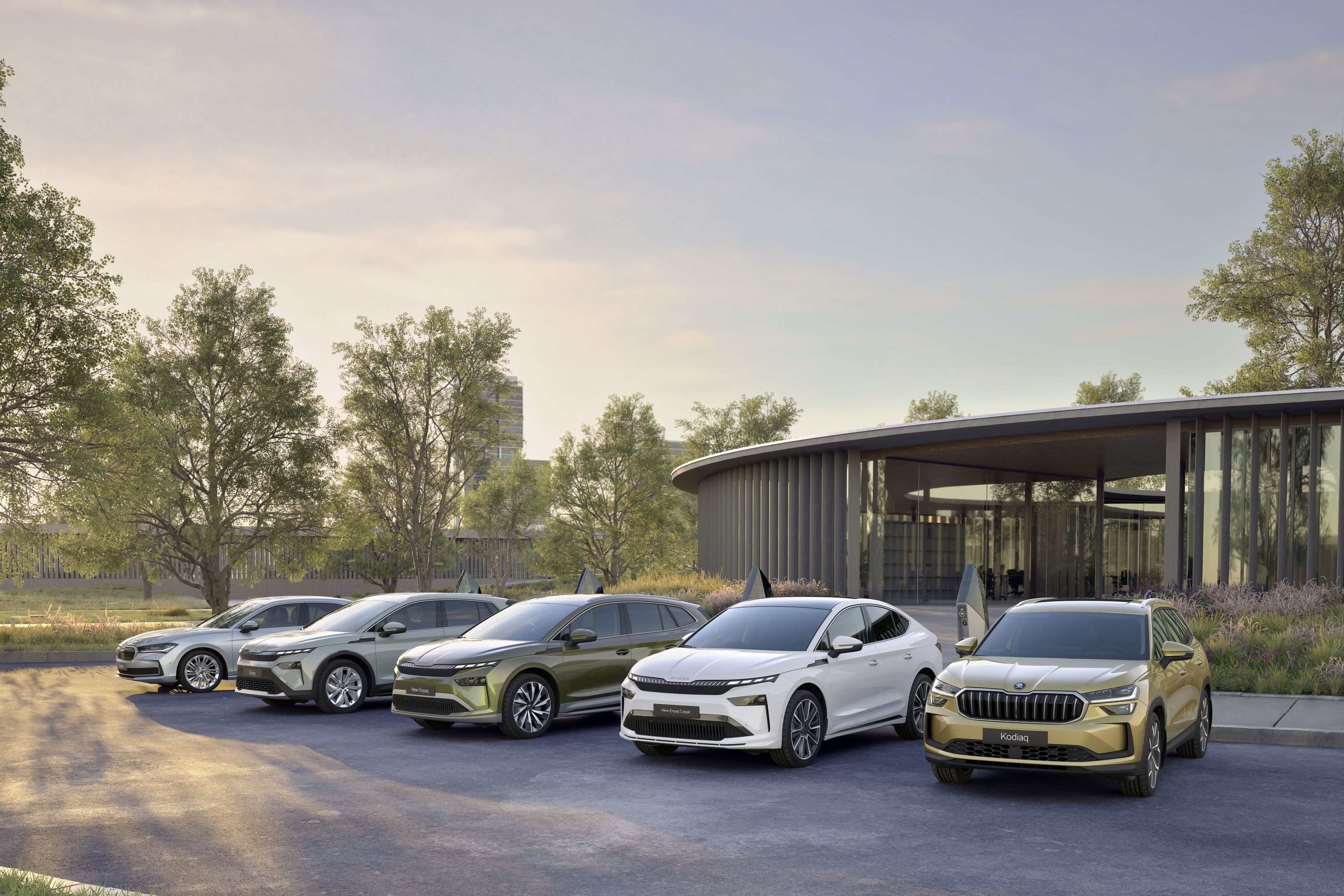 V vrsti na parkirišču stoji pet avtomobilov različnih modelov. V ozadju je sodobna stavba z velikimi steklenimi okni, okoli katere rastejo drevesa. Spredaj je travnato območje osvetljeno z jutranjo svetlobo.