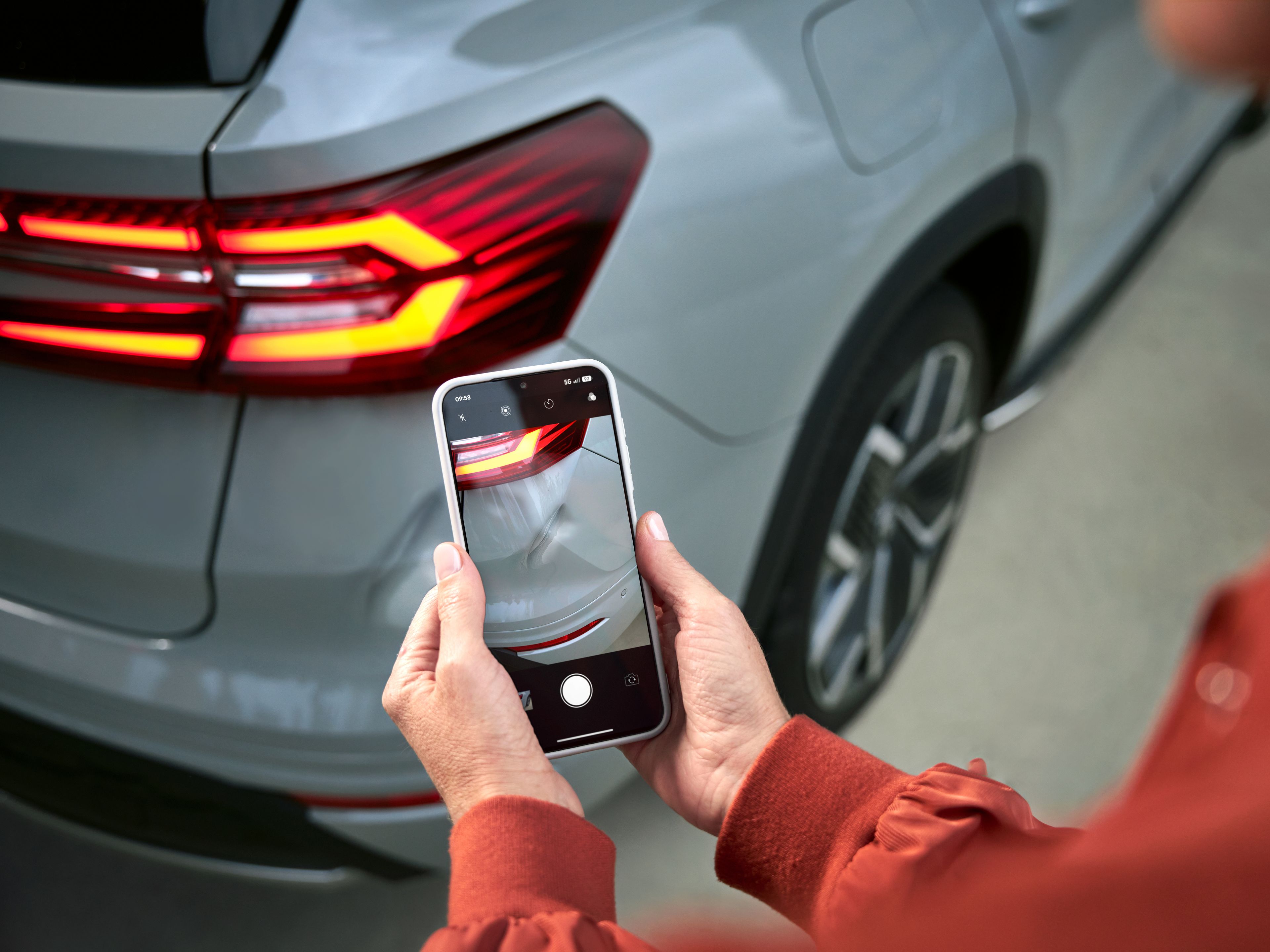 Stranka v roki drži mobitel in gleda sliko poškodbe bočnega dela vozila