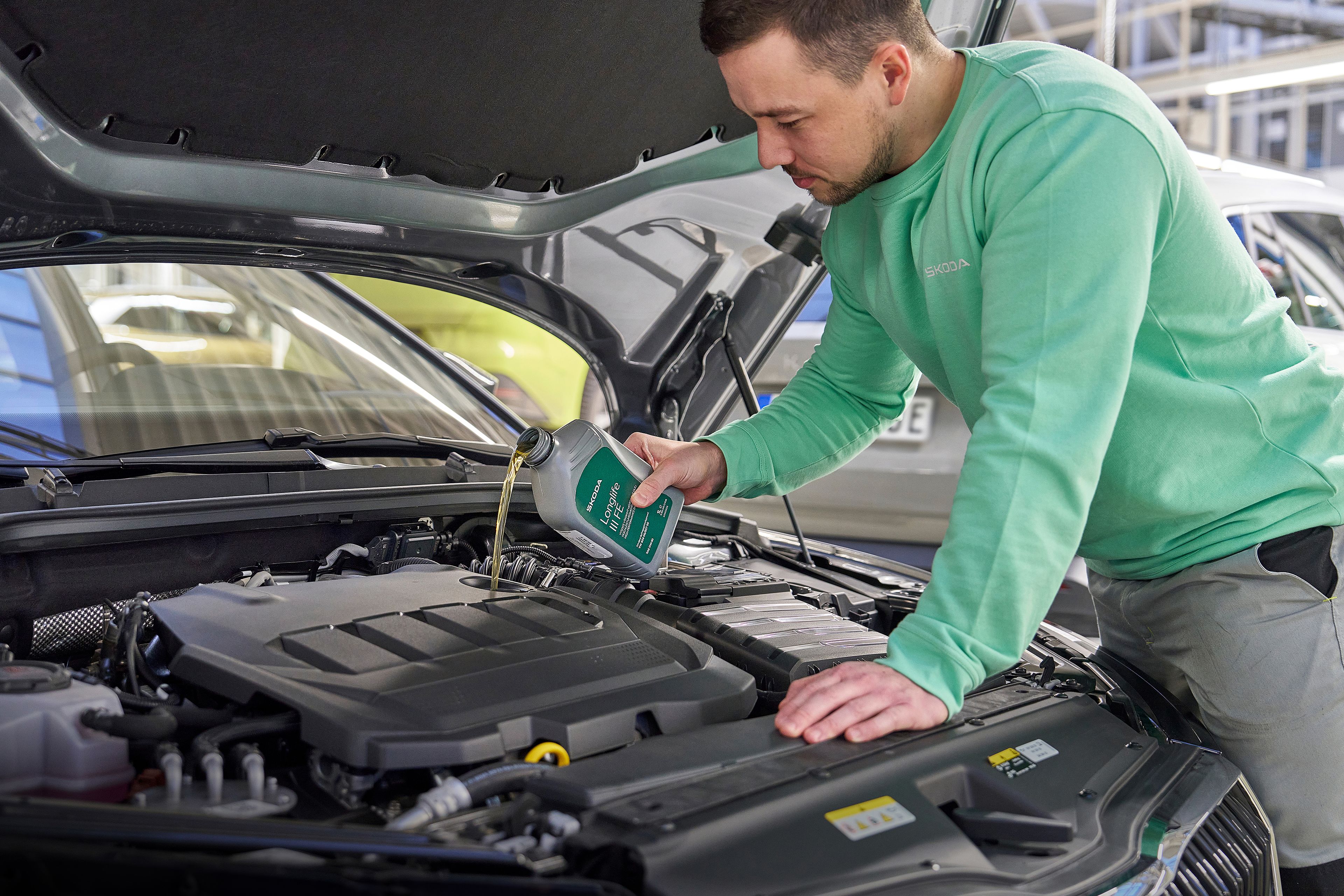 Oseba v delovni obleki doliva motorno olje v avtomobilski motor pod odprto pokrovom.