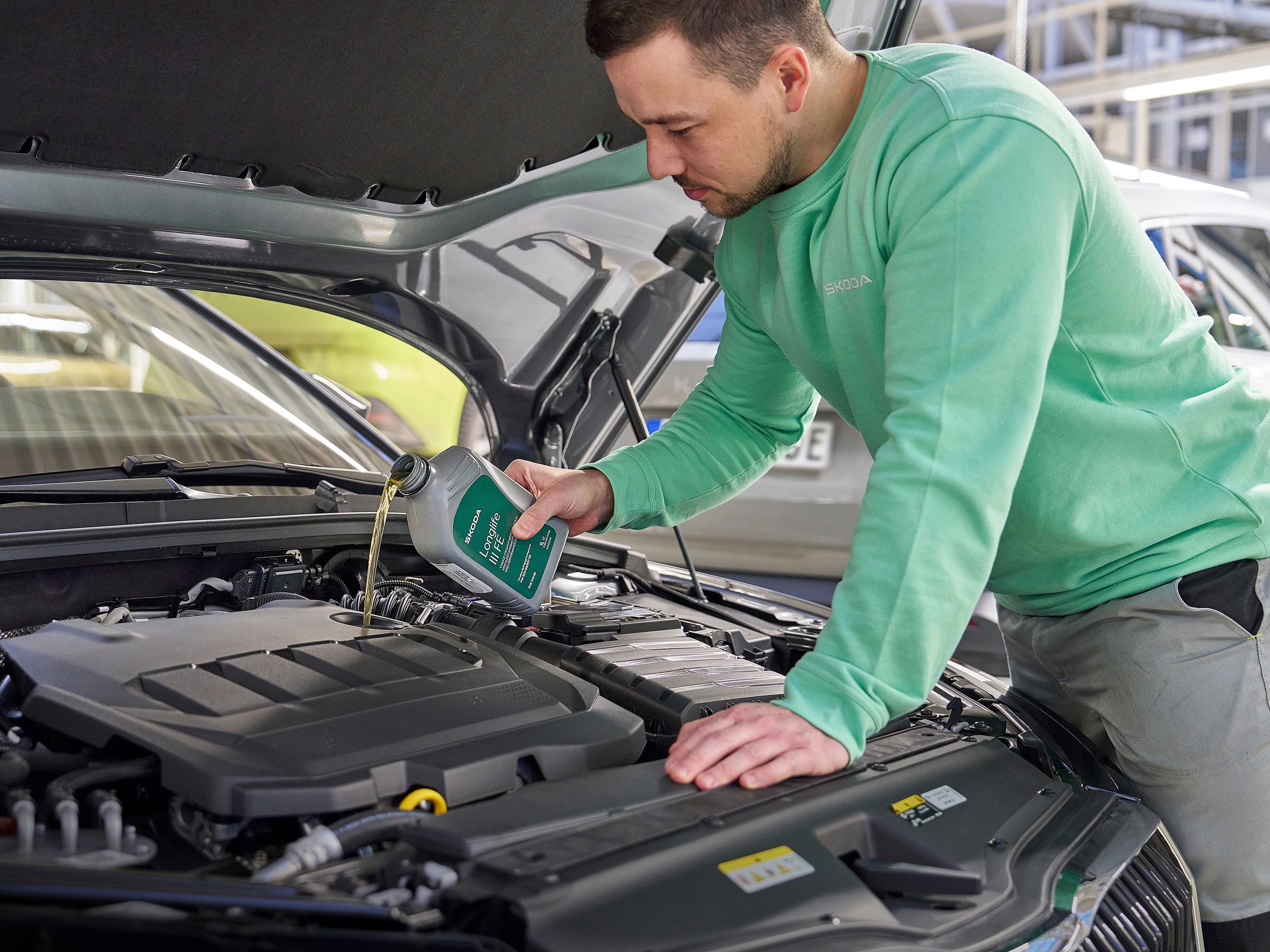 Oseba v delovni obleki doliva motorno olje v avtomobilski motor pod odprto pokrovom.