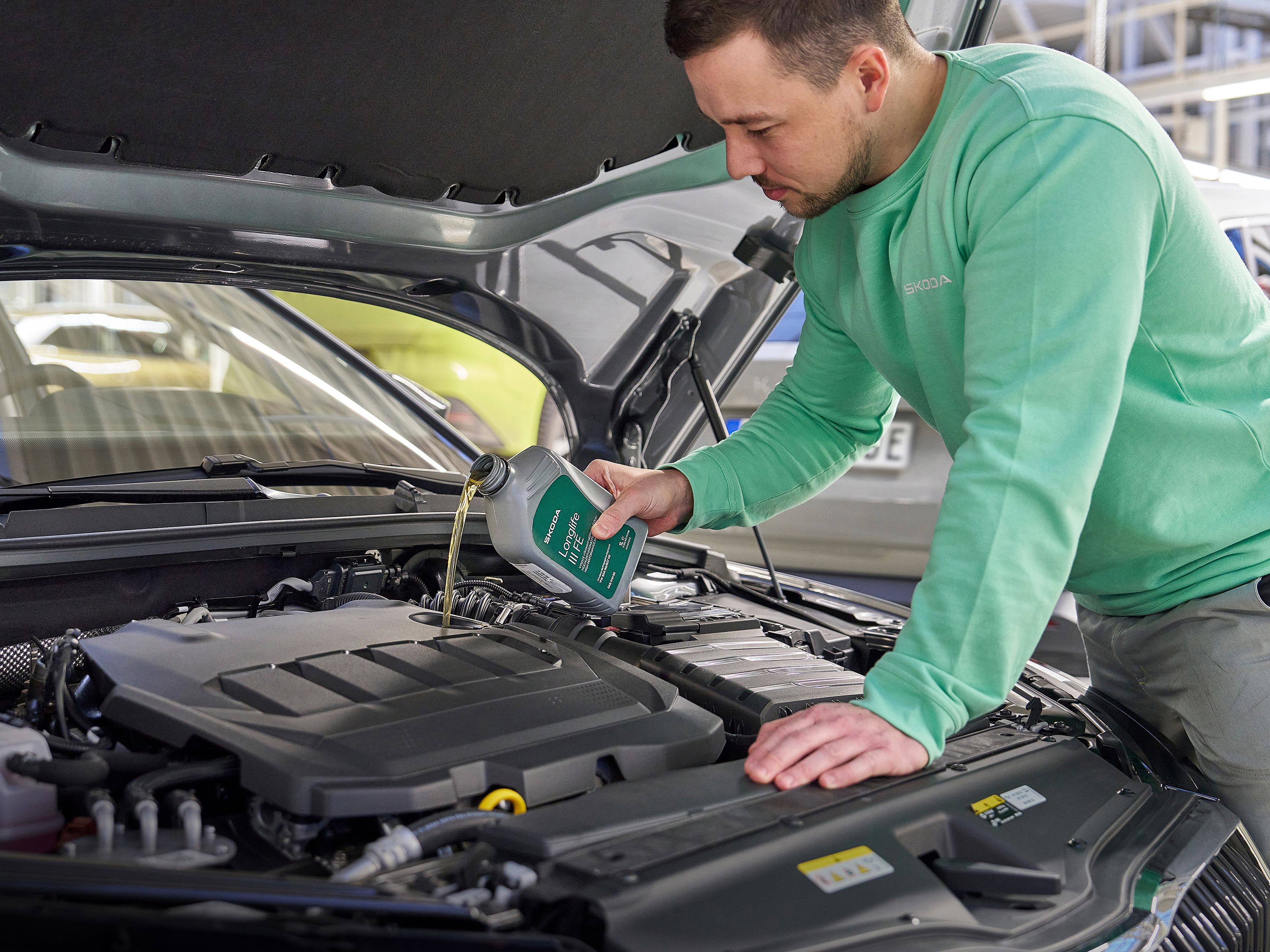 Oseba v delovni obleki doliva motorno olje v avtomobilski motor pod odprto pokrovom.