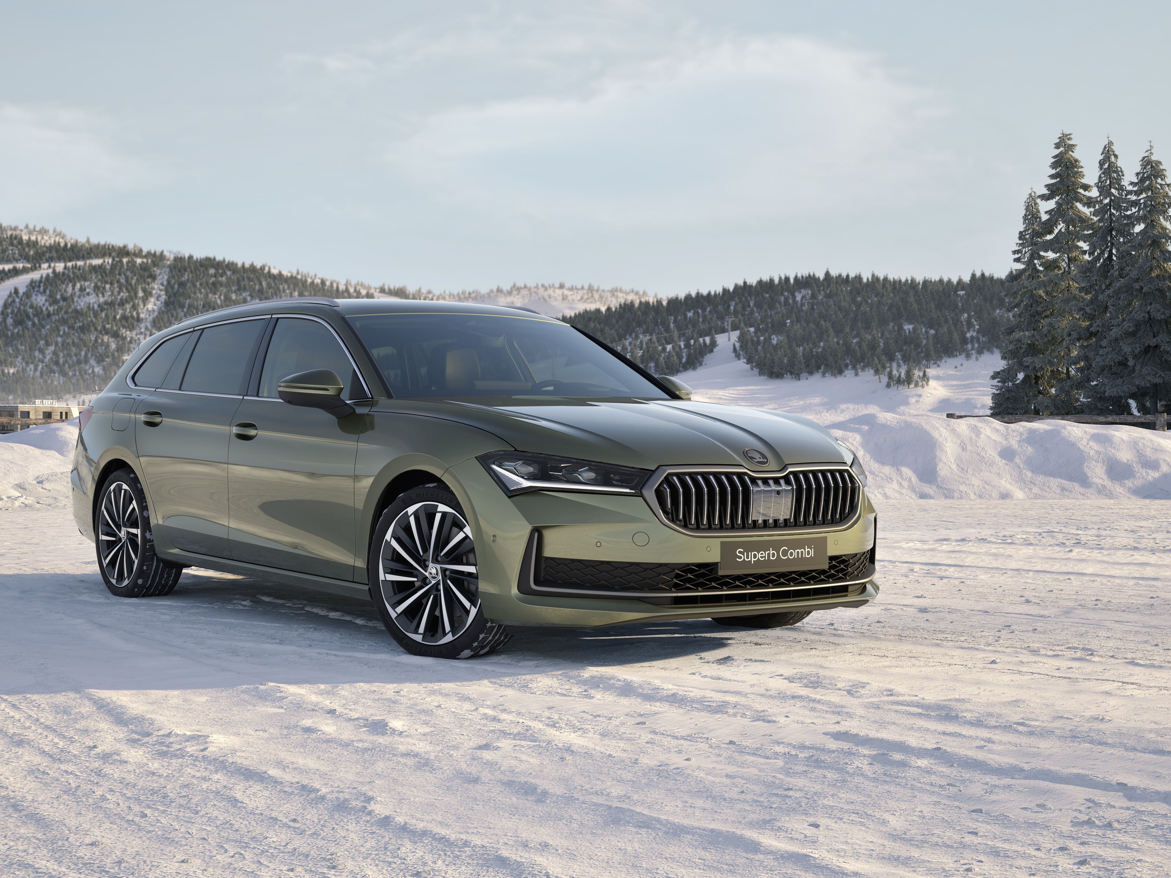 Škoda Superb Combi zelene barve, parkiran na zasneženi cesti. V ozadju so zasnežena drevesa in hribi.