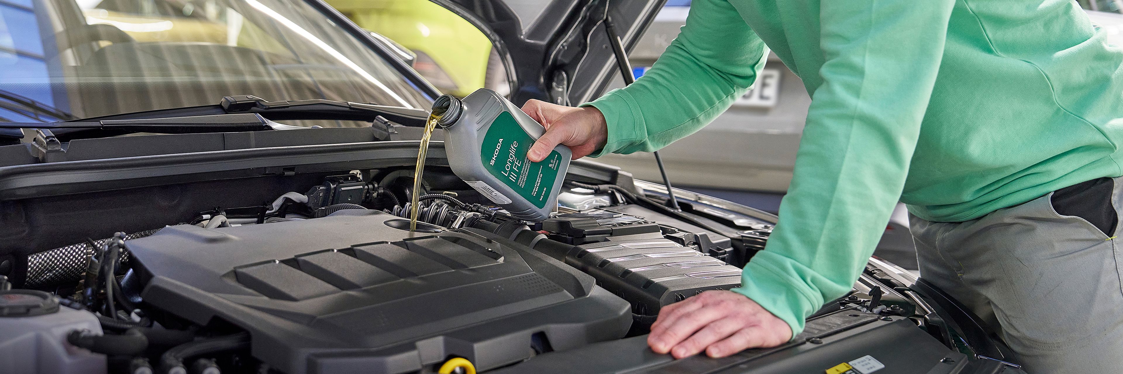 Oseba v delovni obleki doliva motorno olje v avtomobilski motor pod odprto pokrovom.